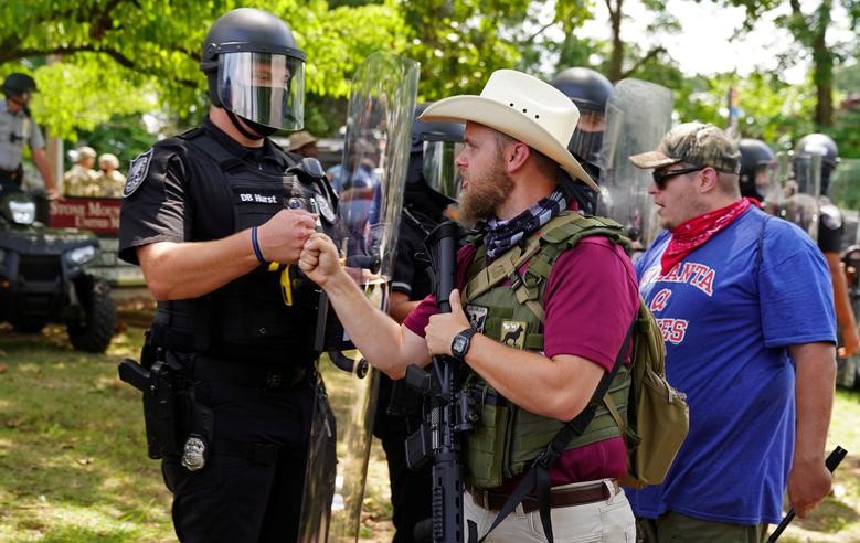 An armed far-right militia member fist-bumps a police officer in riot gear as various militia groups stage rallies at the Confederate memorial at Stone Mountain, Georgia. REUTERS/Elijah Nouvelage